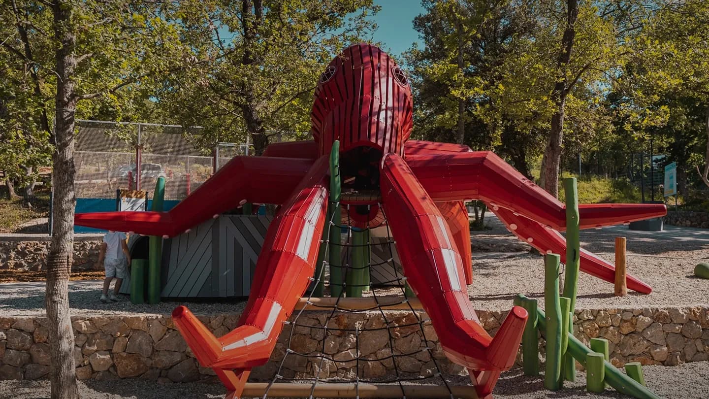 The red timber octopus structure at Glavotok Campsite, seen from the front, with its rope net entrance and dry-stone wall base.