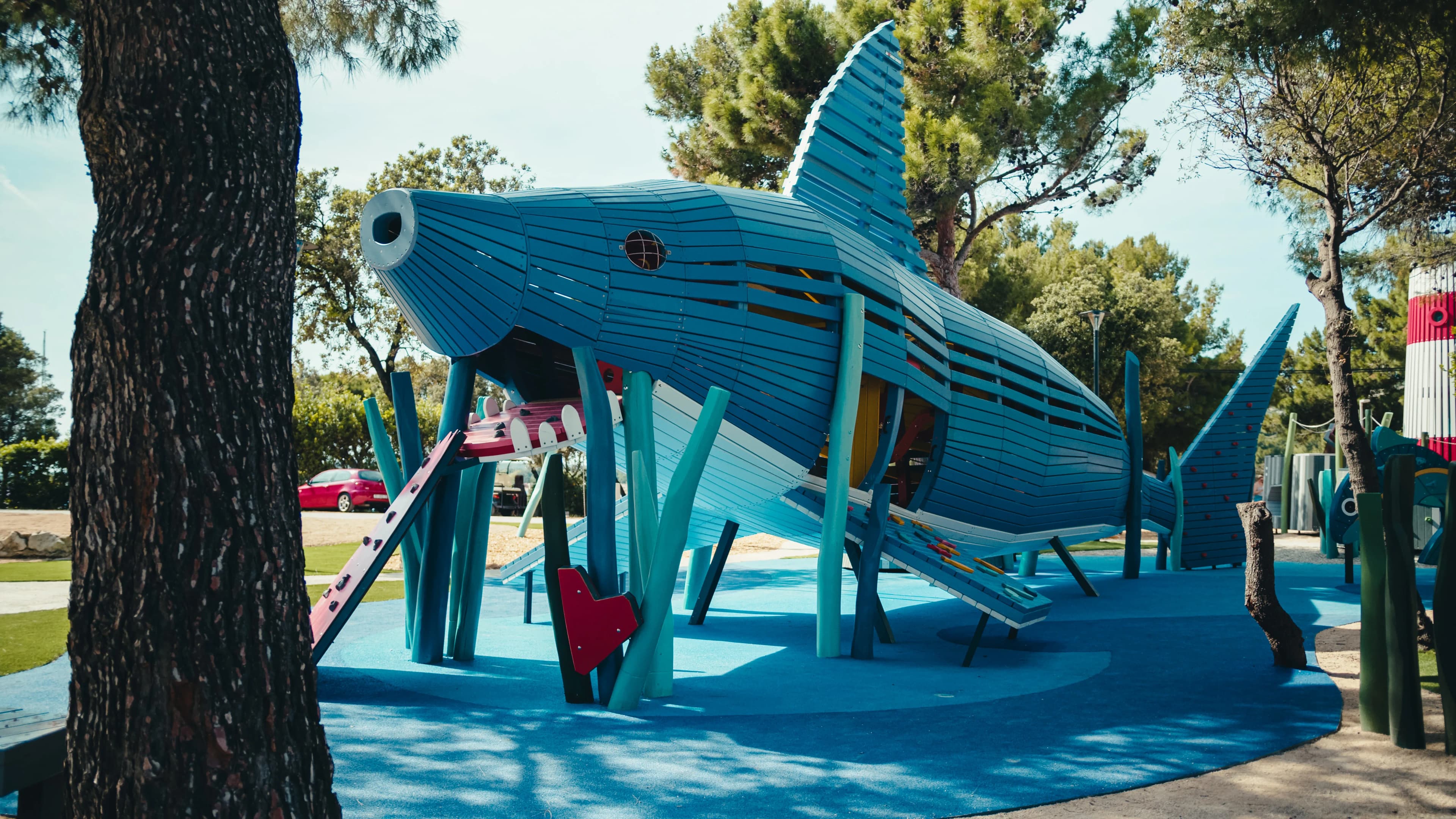 The timber shark structure at Sea World, seen from the side among pine trees, with its climbing ramp and tail fin visible.