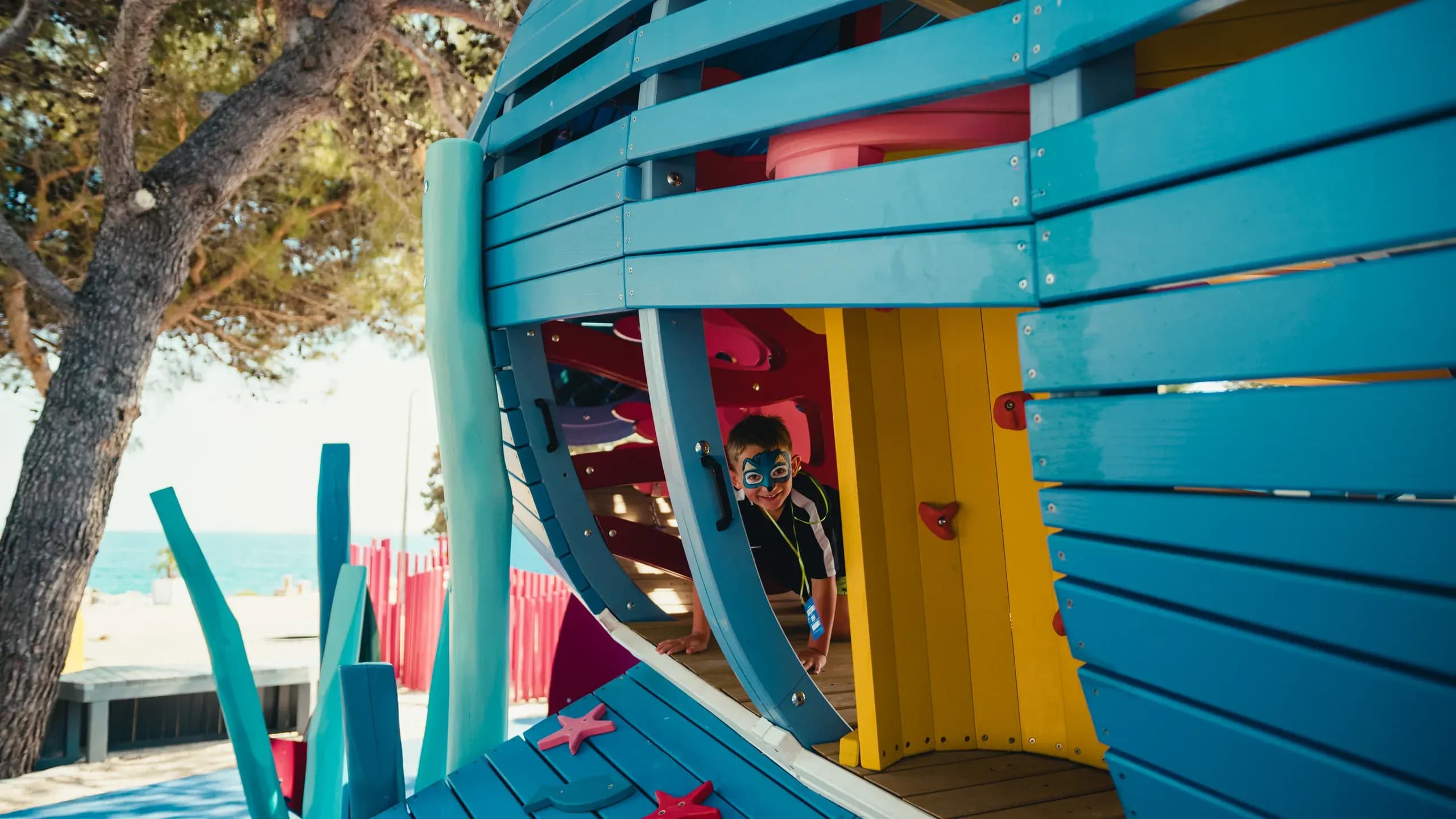 A child looking out from inside the shark structure at Sea World, with the slide and climbing wall visible.