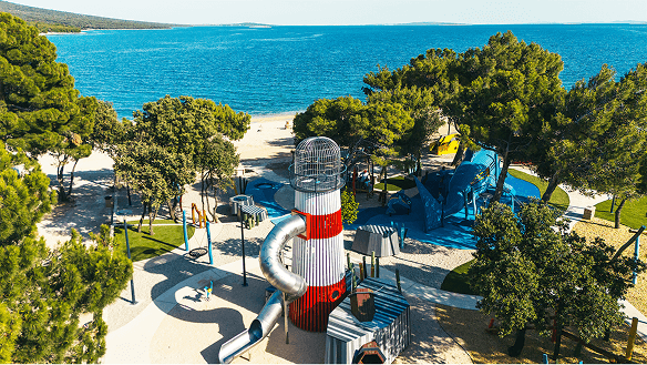 Aerial view of the Sea World playground showing the lighthouse tower and the timber shark structure among pine trees.