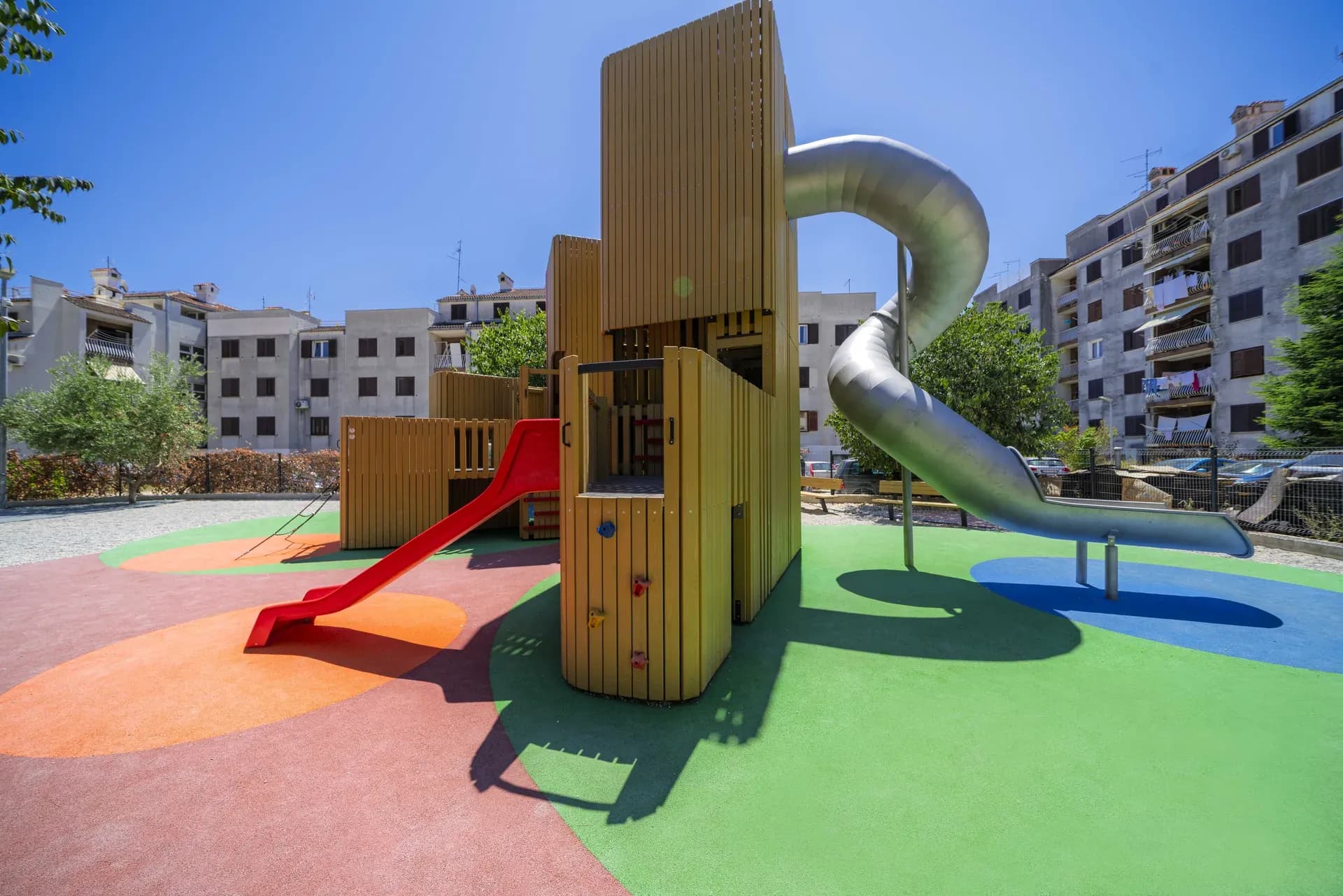 Ground level view of the Urban Structure playground in Trogir, with the red slide and climbing wall.