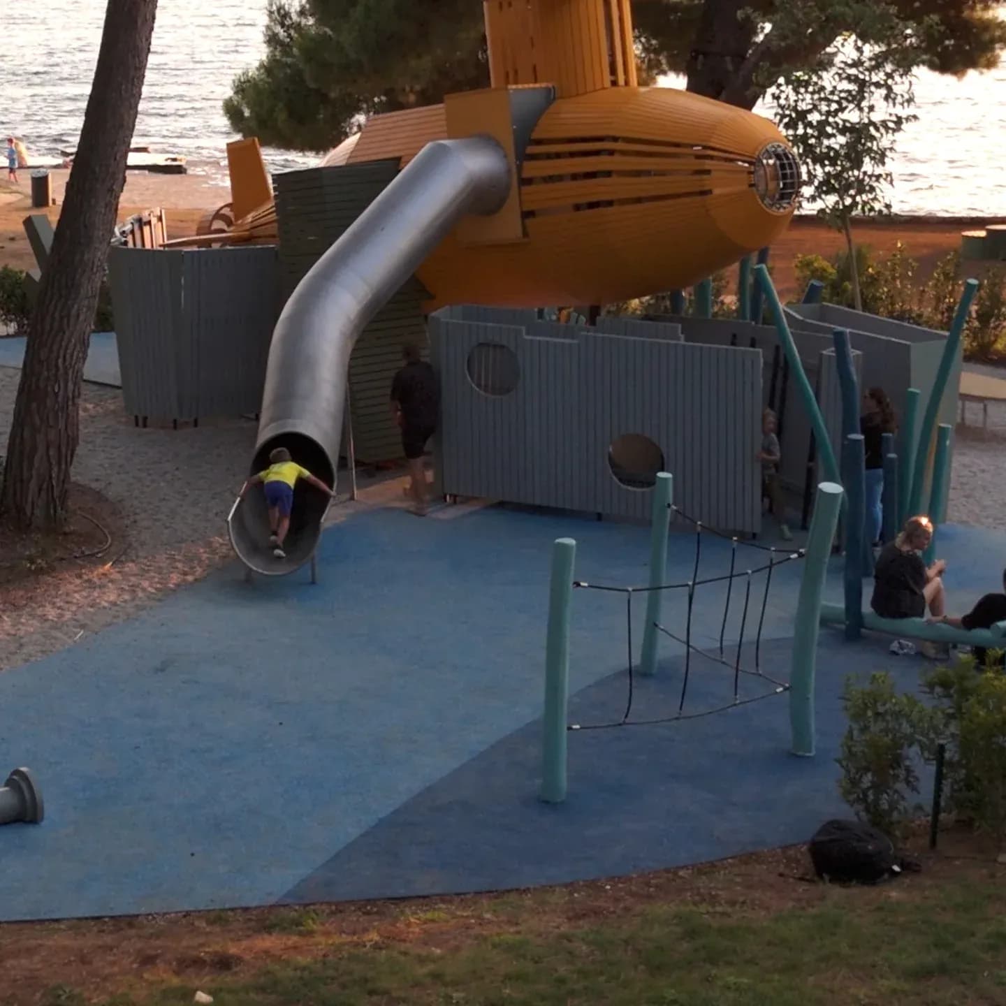 A child coming out of the stainless steel tube slide that runs from the yellow submarine down to the blue surfacing, Yellow Submarine playground in Poreč