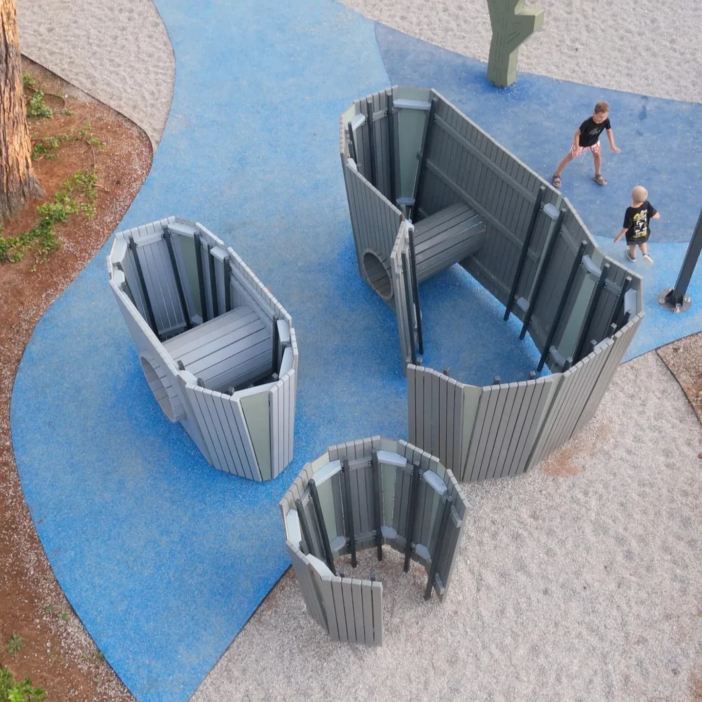 Aerial view of the curved stone labyrinth walls with hidden passages and portholes, two children playing between them, Yellow Submarine playground in Poreč