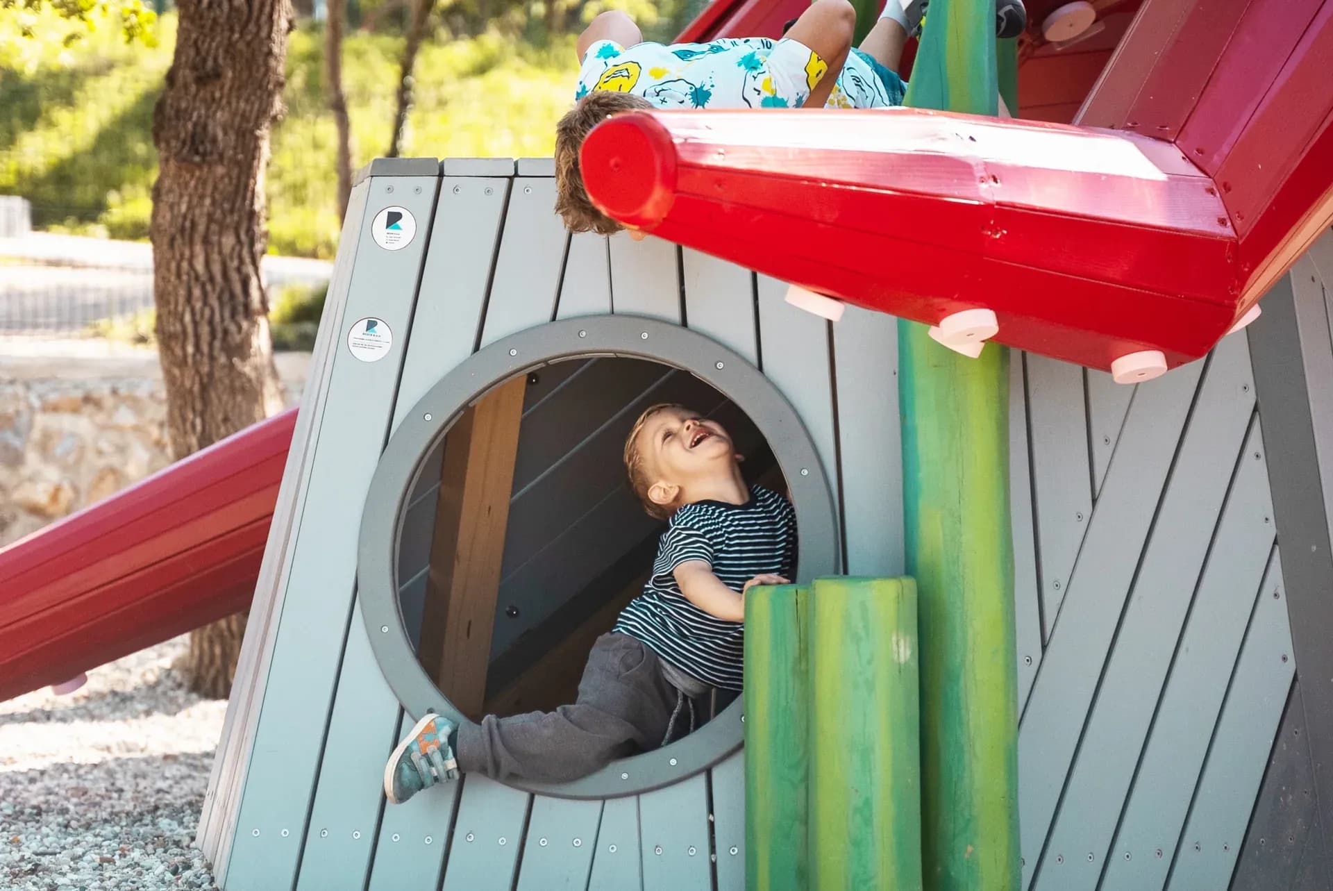 A companion climbing structure beside the octopus at Glavotok, with a porthole window and slide.