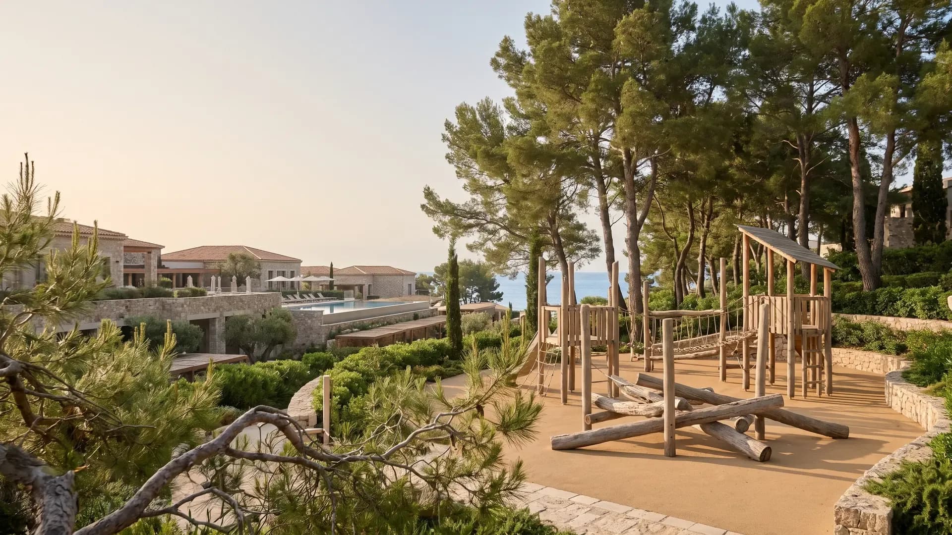 Natural timber playground integrated into a Mediterranean resort with pine trees and sea view