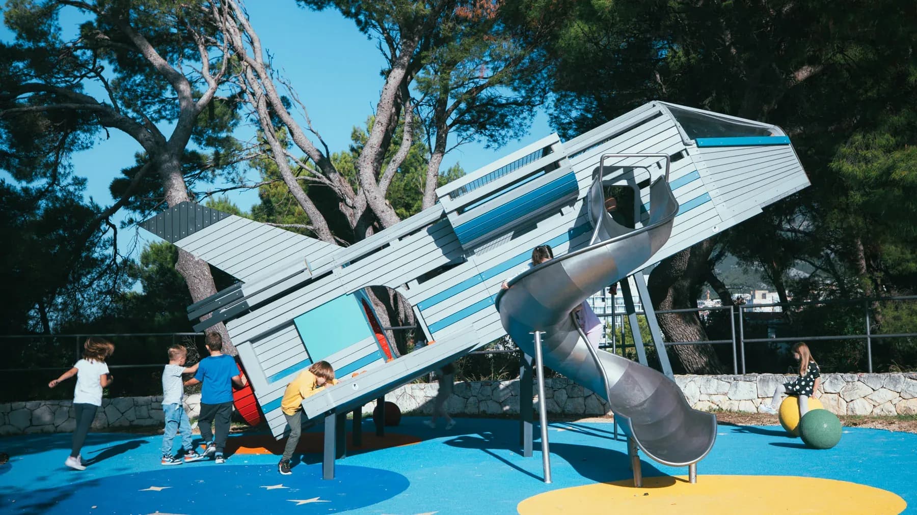 Children playing on a custom rocket-themed playground with a spiral slide and space-themed safety surfacing